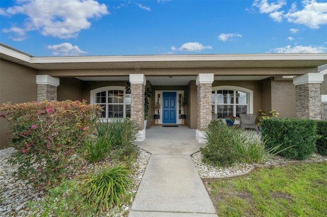 property entrance with stucco siding, stone siding, and covered porch