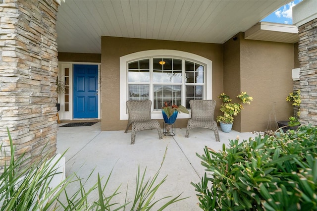 property entrance with stone siding, stucco siding, and covered porch