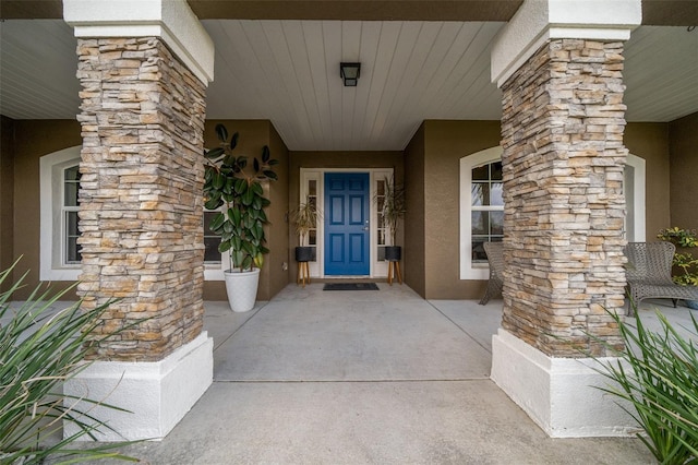 entrance to property featuring stucco siding, stone siding, and covered porch