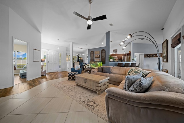 living area featuring a ceiling fan, visible vents, baseboards, high vaulted ceiling, and tile patterned floors