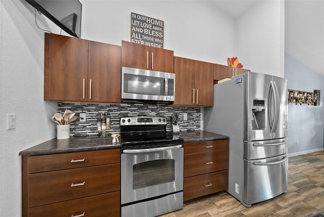 kitchen featuring backsplash, dark stone counters, vaulted ceiling, light wood-style floors, and stainless steel appliances