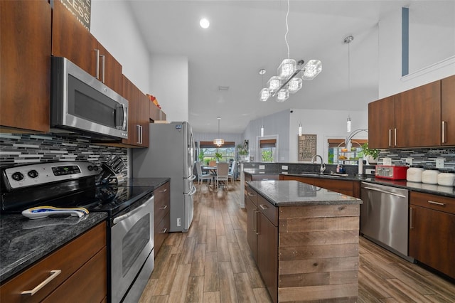 kitchen with a sink, wood finished floors, stainless steel appliances, a peninsula, and decorative backsplash