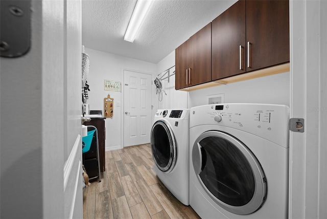 clothes washing area with cabinet space, washer and dryer, a textured ceiling, and light wood-type flooring