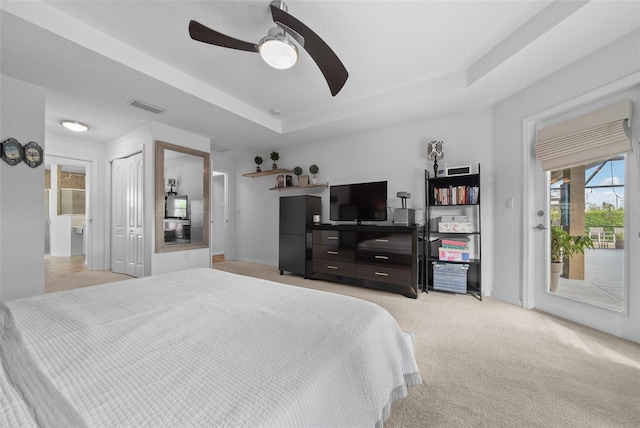 bedroom featuring a ceiling fan, visible vents, a tray ceiling, access to exterior, and light carpet