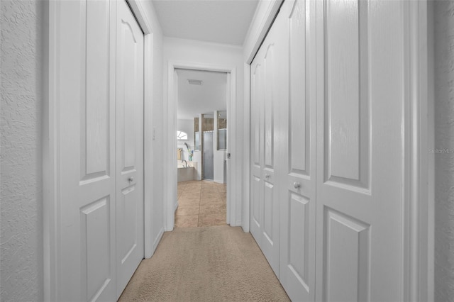 corridor featuring light carpet, light tile patterned floors, and a textured wall