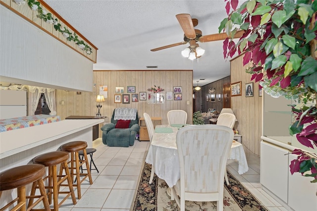 dining room with light tile patterned floors, a textured ceiling, ceiling fan, and wooden walls