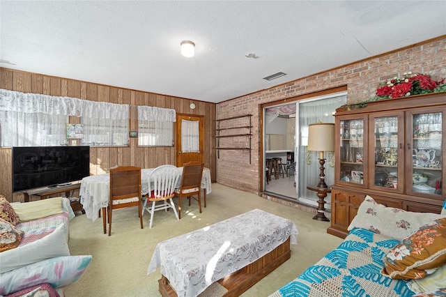 carpeted living room featuring wood walls, visible vents, brick wall, and a textured ceiling