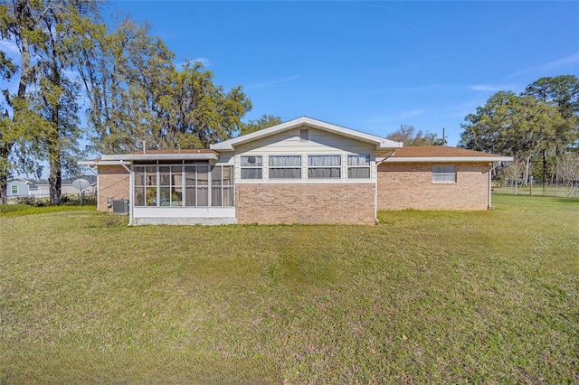 rear view of house featuring a yard, brick siding, cooling unit, and a sunroom