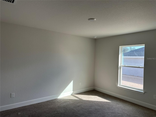 spare room featuring carpet flooring, visible vents, a textured ceiling, and baseboards