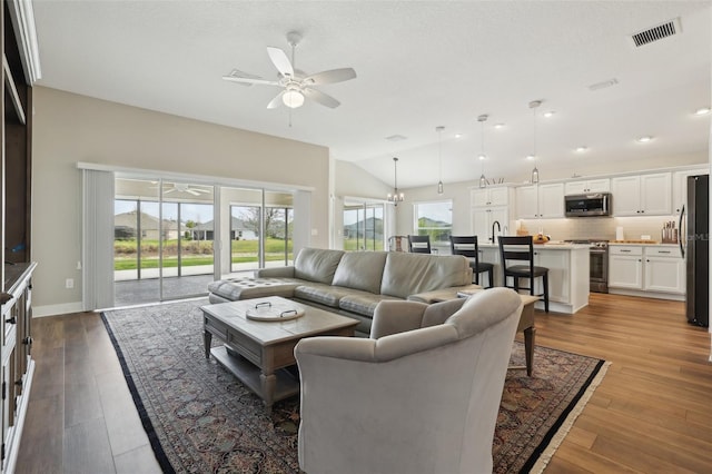 living room featuring visible vents, baseboards, vaulted ceiling, wood finished floors, and a ceiling fan