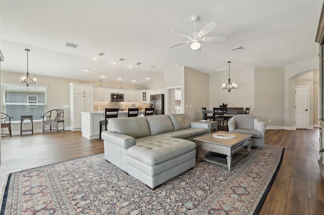 living area featuring arched walkways, visible vents, dark wood finished floors, and ceiling fan with notable chandelier