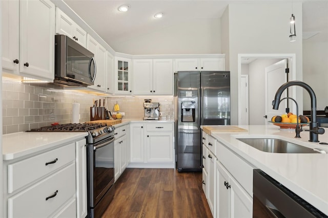 kitchen with dark wood finished floors, vaulted ceiling, decorative backsplash, stainless steel appliances, and a sink