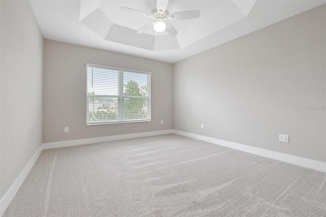 unfurnished room with a tray ceiling, light colored carpet, and baseboards