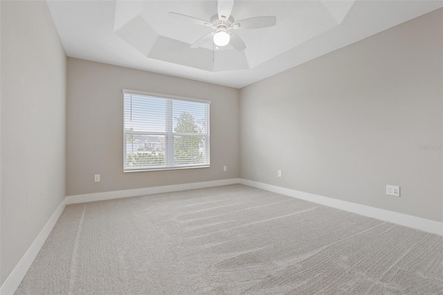 unfurnished room with light carpet, ceiling fan, baseboards, and a tray ceiling