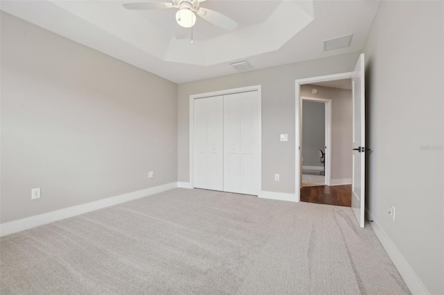 unfurnished bedroom with a tray ceiling, carpet flooring, baseboards, and visible vents