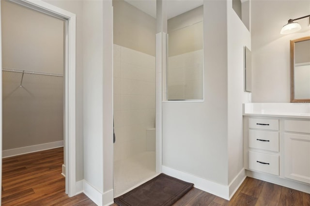 bathroom with wood finished floors, vanity, baseboards, walk in shower, and a spacious closet