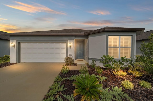 view of front of home with stucco siding, an attached garage, concrete driveway, and roof with shingles