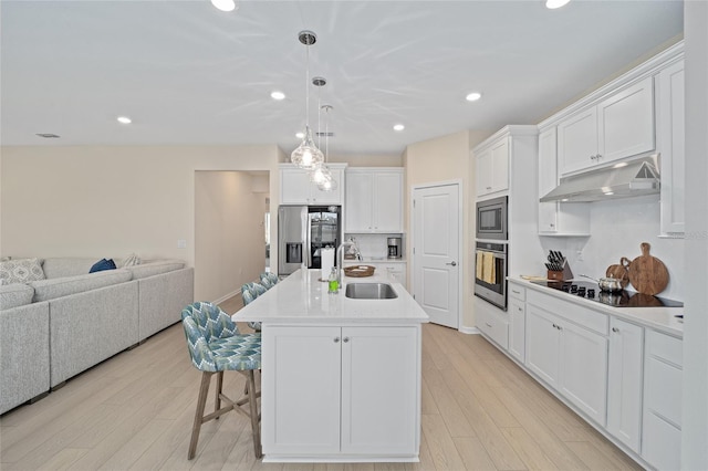 kitchen with under cabinet range hood, open floor plan, light wood-style flooring, stainless steel appliances, and a sink