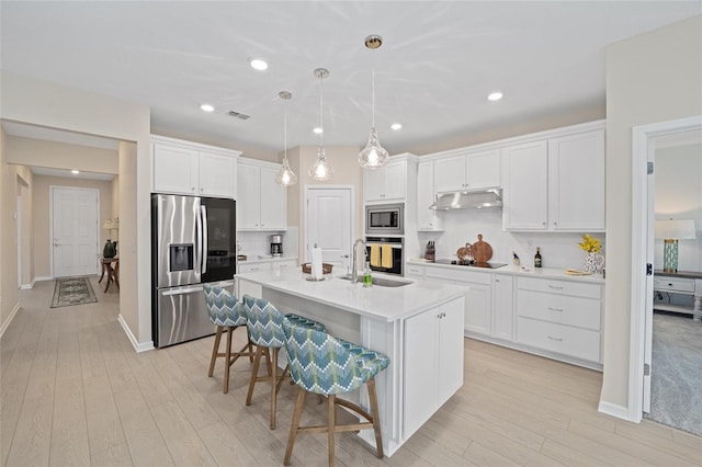 kitchen with under cabinet range hood, a sink, appliances with stainless steel finishes, white cabinets, and light countertops