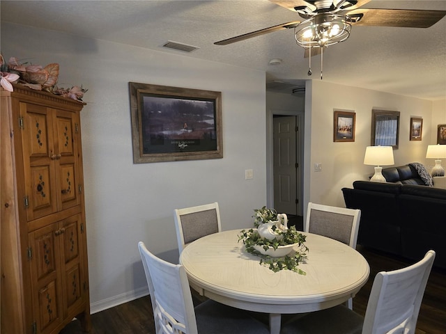 dining room with a ceiling fan, baseboards, visible vents, dark wood finished floors, and a textured ceiling