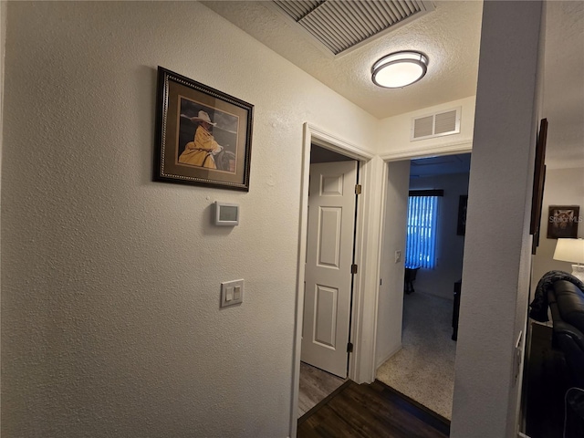 hall featuring dark wood finished floors, a textured wall, visible vents, and a textured ceiling