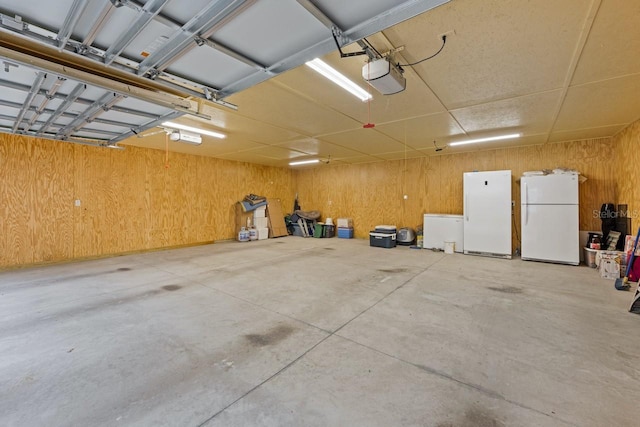 garage featuring wooden walls, refrigerator, a garage door opener, and freestanding refrigerator