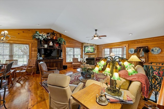 dining room with wood walls, lofted ceiling, ceiling fan with notable chandelier, a fireplace, and wood-type flooring