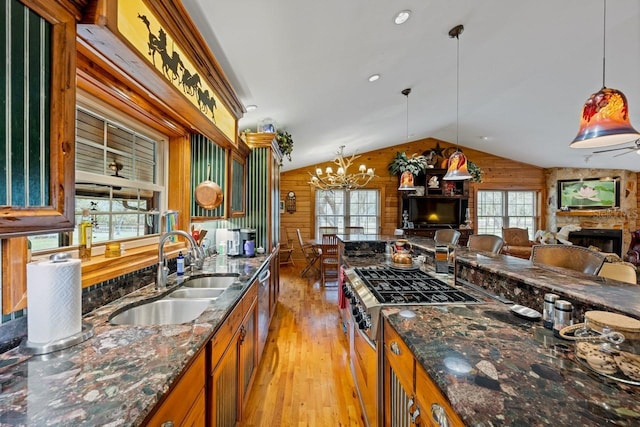 kitchen featuring a sink, a stone fireplace, wood walls, and vaulted ceiling