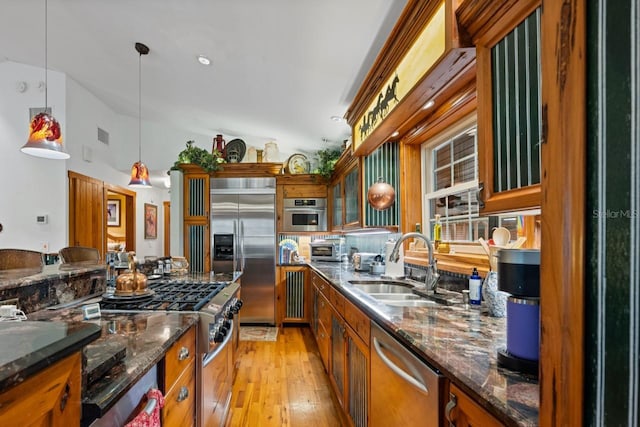 kitchen featuring brown cabinetry, lofted ceiling, a sink, hanging light fixtures, and appliances with stainless steel finishes