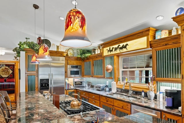 kitchen with a sink, appliances with stainless steel finishes, dark stone countertops, and pendant lighting