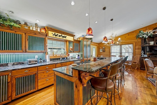 kitchen featuring an inviting chandelier, a sink, wood walls, a kitchen breakfast bar, and light wood-type flooring