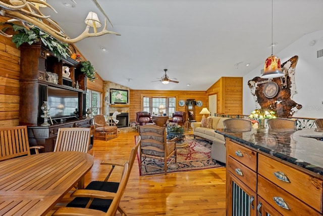 dining space featuring wooden walls, light wood-style flooring, a stone fireplace, and lofted ceiling