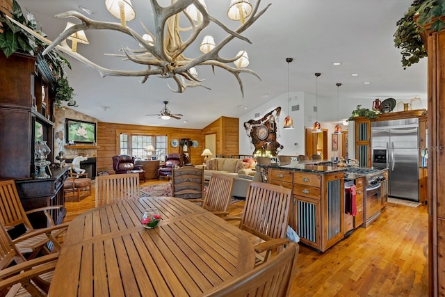 dining area with a stone fireplace, light wood-style flooring, wooden walls, and vaulted ceiling