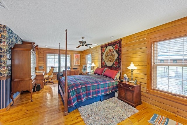 bedroom featuring wooden walls, light wood finished floors, and a textured ceiling