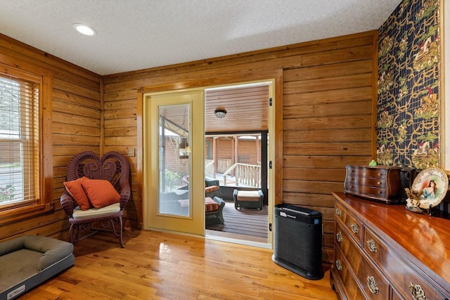 sitting room featuring light wood finished floors, wooden walls, and a textured ceiling