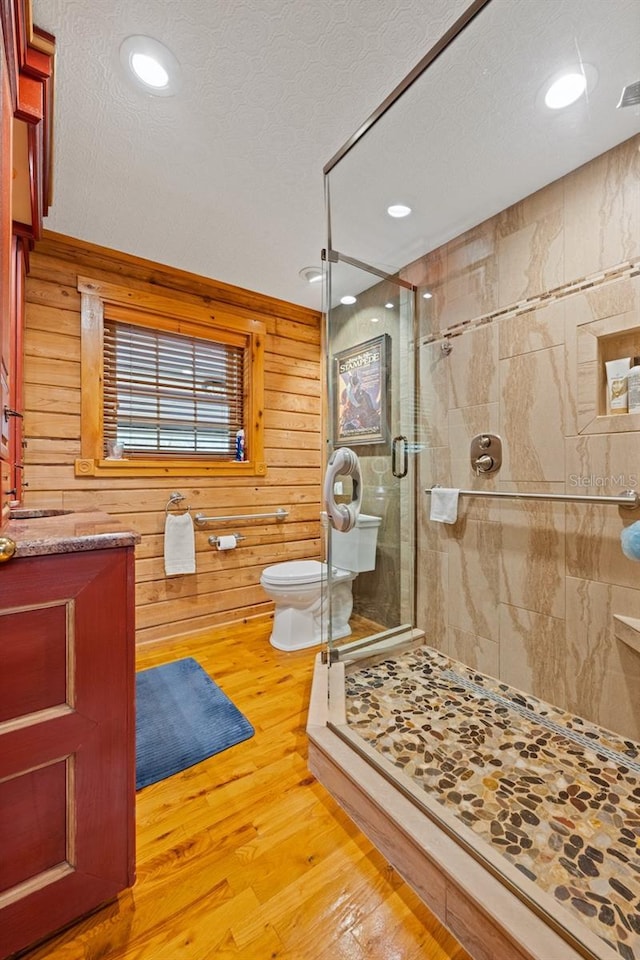 bathroom featuring toilet, a stall shower, a textured ceiling, wood finished floors, and wood walls