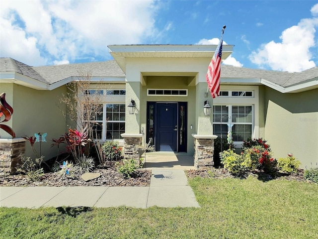 view of exterior entry featuring stone siding, stucco siding, and a shingled roof