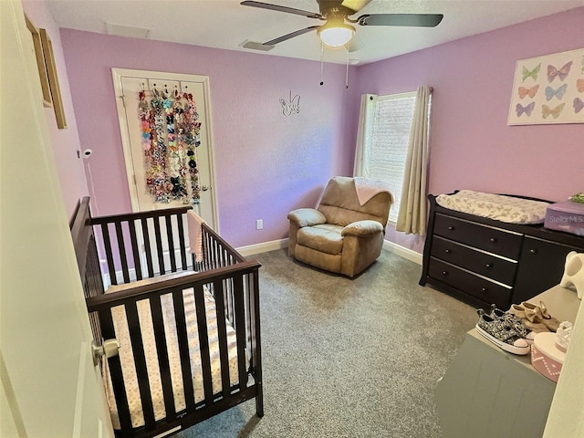 carpeted bedroom featuring a crib, visible vents, a ceiling fan, and baseboards