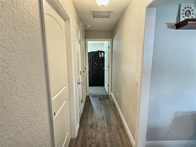 hall with visible vents, baseboards, dark wood-style floors, and a textured wall