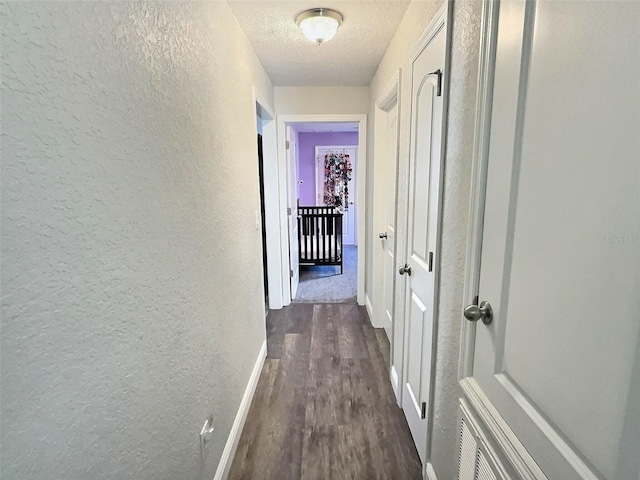 hallway featuring dark wood finished floors, a textured wall, baseboards, and a textured ceiling