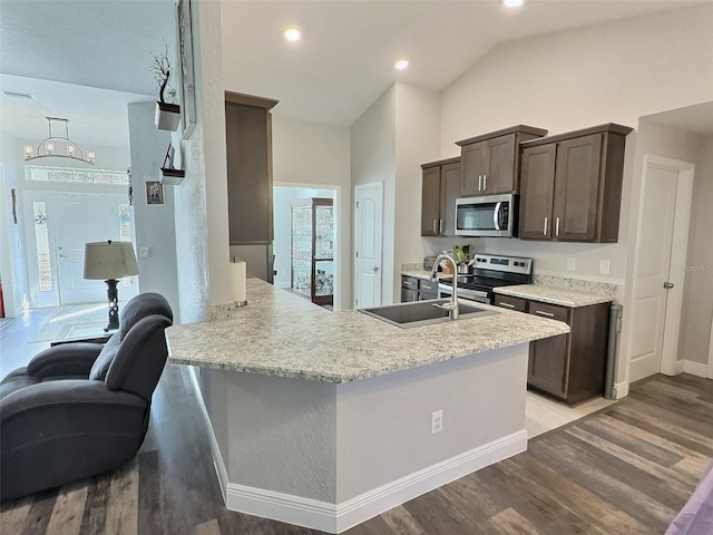 kitchen with a peninsula, a sink, stainless steel appliances, dark brown cabinets, and light wood-type flooring