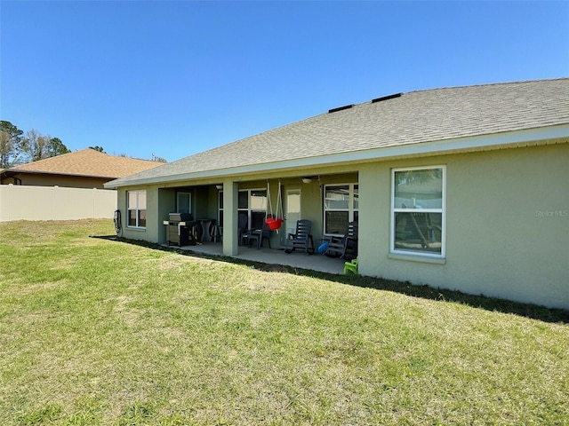 rear view of house with fence, roof with shingles, stucco siding, a yard, and a patio area