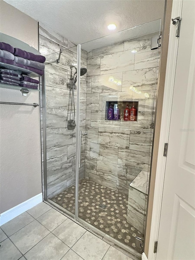 bathroom with tile patterned flooring, a shower stall, baseboards, and a textured ceiling