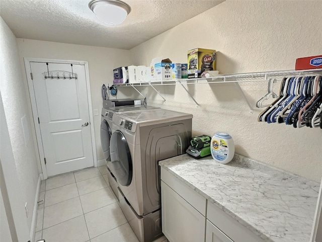 laundry area with washer and dryer, a textured ceiling, light tile patterned floors, baseboards, and a textured wall