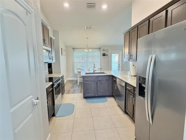 1034 SE 65th Cir, Ocala, FL 34472 - kitchen with appliances with stainless steel finishes, a peninsula, light tile patterned flooring, dark brown cabinets, and decorative light fixtures