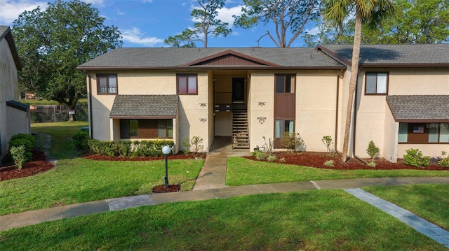 townhome / multi-family property with stairway, stucco siding, and a front lawn