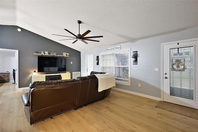 living room featuring a ceiling fan, baseboards, light wood finished floors, vaulted ceiling, and a textured ceiling