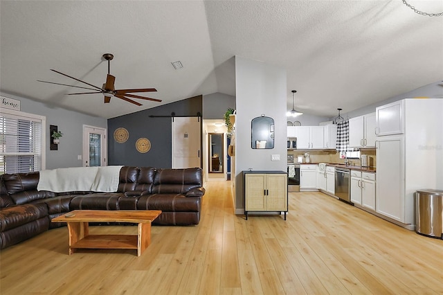 living room with a ceiling fan, visible vents, light wood-style flooring, vaulted ceiling, and a barn door