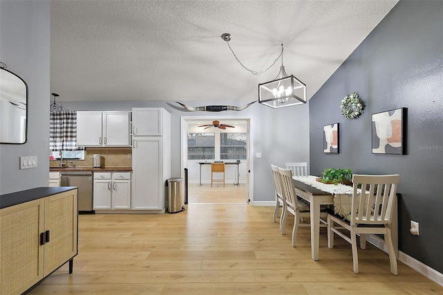 dining area featuring baseboards, light wood-style flooring, vaulted ceiling, a textured ceiling, and ceiling fan with notable chandelier