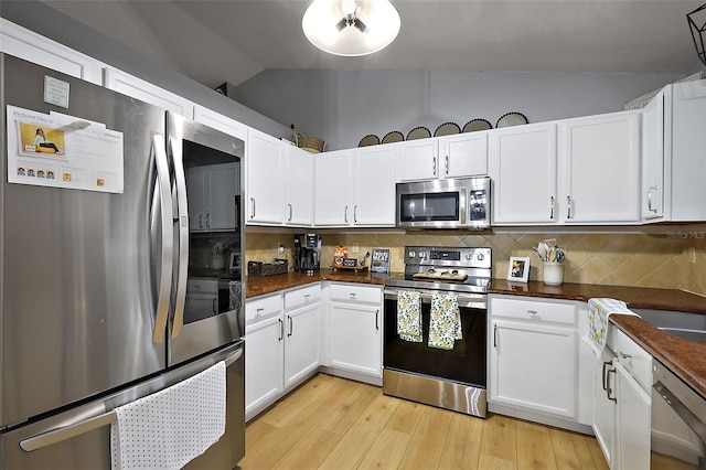 kitchen featuring dark countertops, lofted ceiling, decorative backsplash, white cabinets, and stainless steel appliances